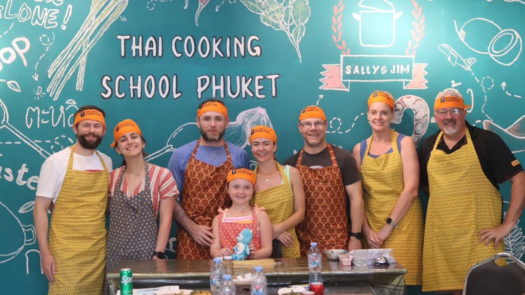 Group in aprons and orange hats at Thai cooking class.